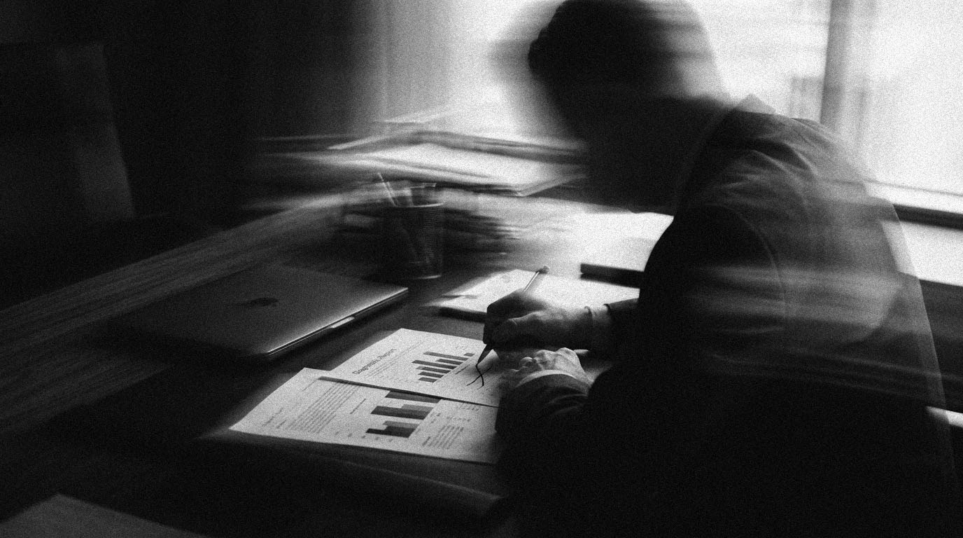 A manager marking a line on a printed diagnostic report with a pen, a closed laptop to the side, in black and white.